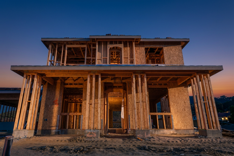 Wood-framed new construction home with lumber on site, protected by a temporary job site alarm